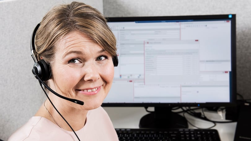 Porträtt av en kvinna med headset framför en datorskärm