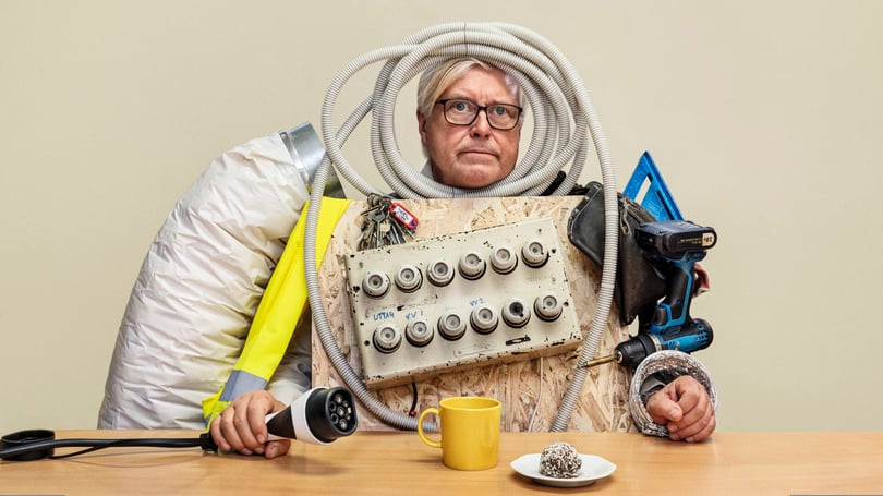 Person utklädd till elkabel med verktyg och kontrollpanel, sittande vid ett bord