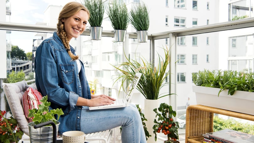 Kvinna som sitter på en inglasad balkong med laptop, omgiven av gröna växter