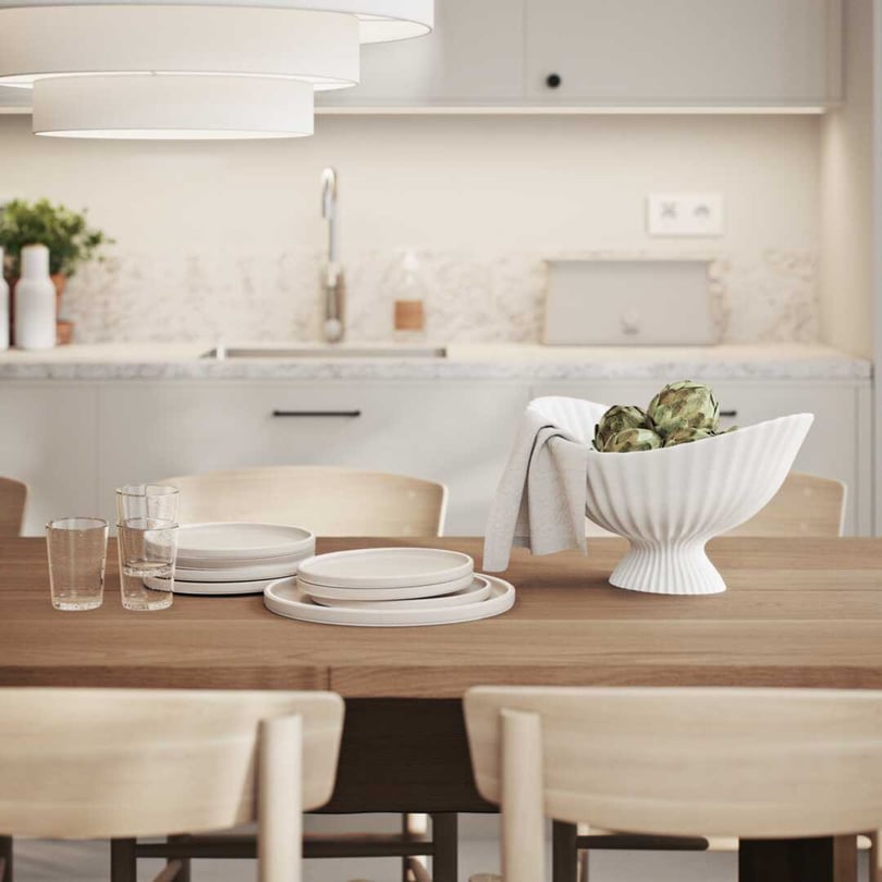 Modern köksinteriör med ett träbord, tallrikar, glas och en vit dekorativ skål med grönsaker. Ljus inredning med marmordetaljer och neutrala färger