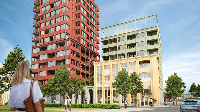 Två moderna flerbostadshus, ett rött och ett gult med gröna inslag, omgivna av träd och människor på en solig dag