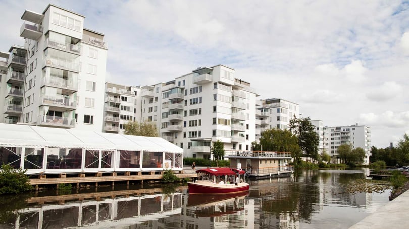 Bostadshus vid vattnet med speglingar i vattenytan och en båt i förgrunden