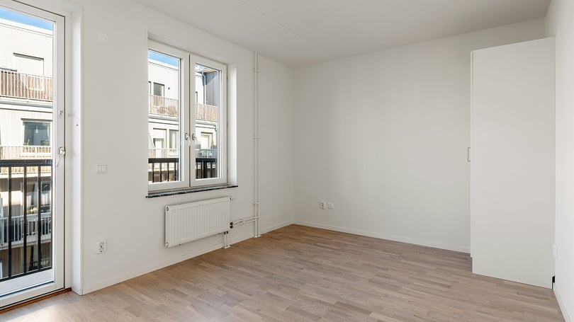 Inflyttningsklar lägenhet med ljusa väggar, trägolv, stort fönster och utgång till balkong
