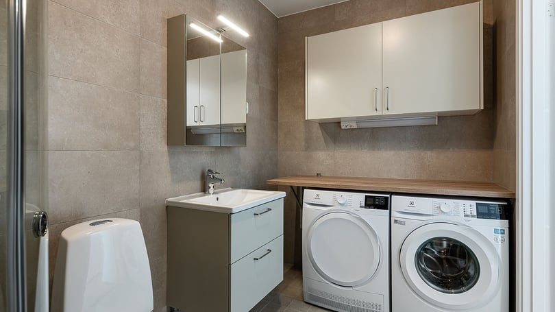 Tvättstuga med tvättmaskin, torktumlare, handfat och förvaringsskåp i modern inredning