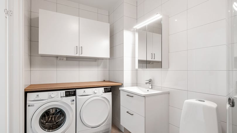Tvättstuga i ljusa toner med tvättmaskin, torktumlare, kommod, spegel och väggskåp
