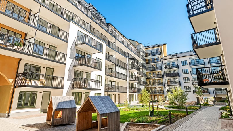Modern bostadsgård med flerbostadshus, balkonger och lekstugor i innergårdsmiljö under klarblå himmel