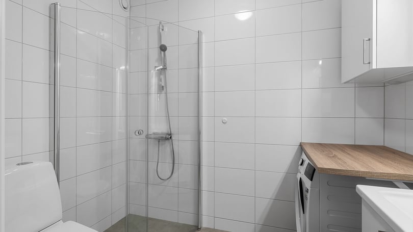 Modernt badrum med duschhörna, vita kaklade väggar och arbetsbänk i ljus trä