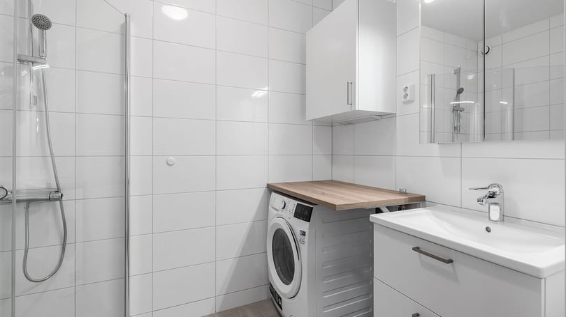 Modernt badrum med dusch, tvättmaskin, handfat och ljusa kakelväggar