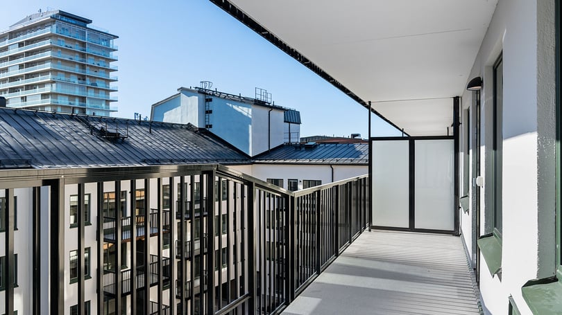 Balkong i en inflyttningsklar lägenhet med svart räcke och utsikt över flerfamiljshus