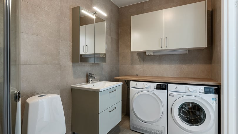 Tvättstuga med tvättmaskin, torktumlare, handfat och förvaringsskåp i modern inredning