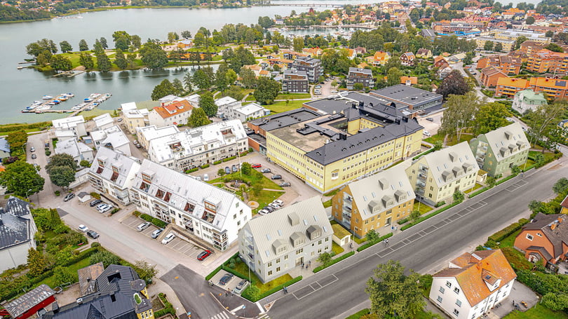 Flygvy över ett bostadsområde vid vatten med flerbostadshus, parkering och båtbrygga