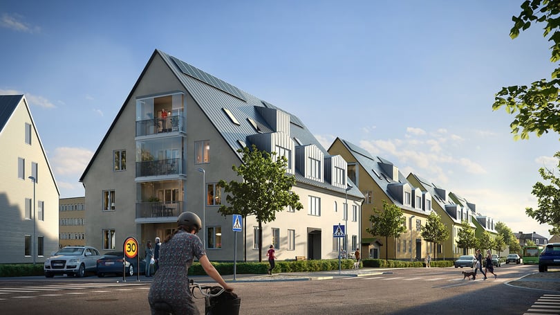 Bostadskvarter med moderna flerbostadshus, balkonger och gröna träd längs gatan. Cyklist i förgrunden och människor som rör sig på trottoaren