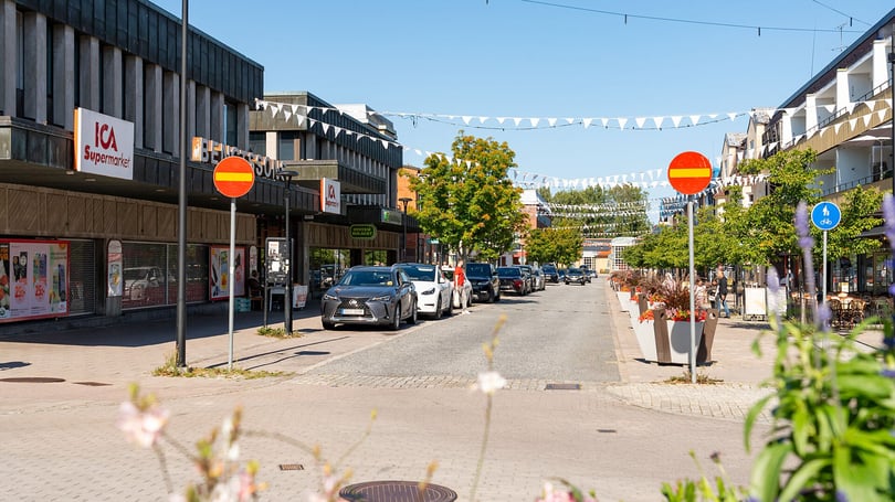 Gågata med butiker, parkerade bilar och blomsterplanteringar i ett bostadsområde