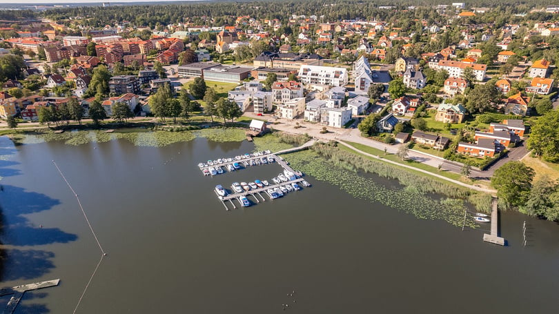 Flygfoto över Mälaren med småbåtshamn, bostäder och grönområden i en tätort