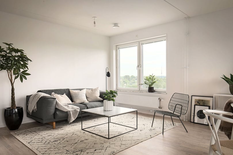 Vardagsrum med grå soffa, soffbord, matta och stora fönster