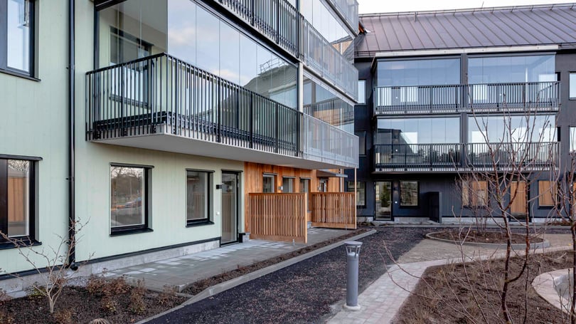 Nybyggda flerfamiljshus med glasade balkonger, modern fasad och ett gårdsområde med stensatta gångvägar
