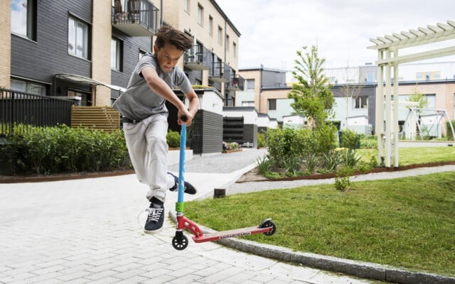 En person som gör ett trick med en röd sparkcykel på en gångväg i ett bostadsområde