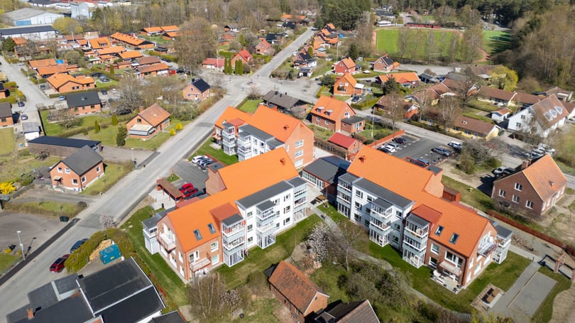 Flygfoto över bostadskvarter med flerbostadshus, villor och parkeringsytor i ett grönt bostadsområde
