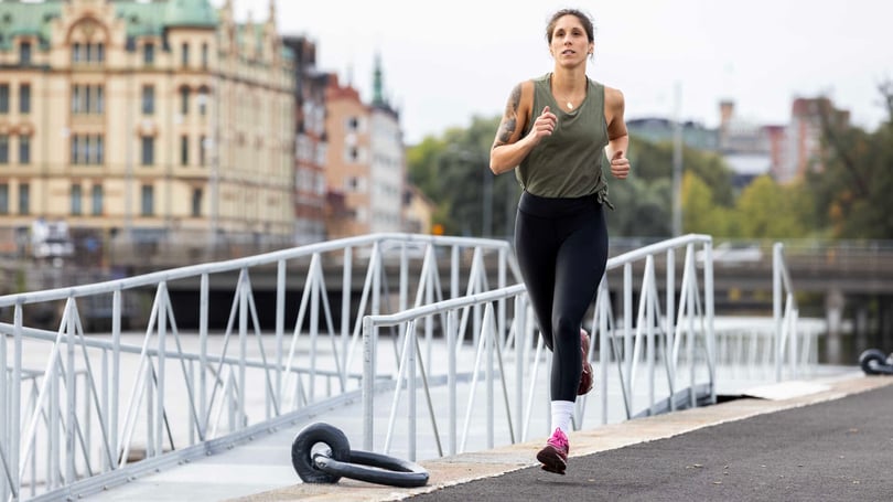 En kvinna springer på en bro i Norrköping, med grönt linne, svarta tights och rosa löparskor