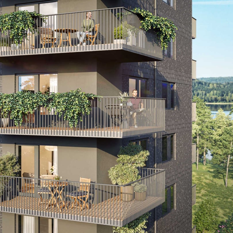 Modern lägenhetsbyggnad med flera balkonger dekorerade med växter och utemöbler, omgiven av grönskande träd och med utsikt över en sjö i bakgrunden
