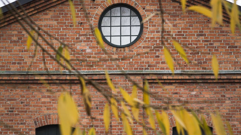 Rött tegelhus i Västerås med runt fönster och gula löv i förgrunden