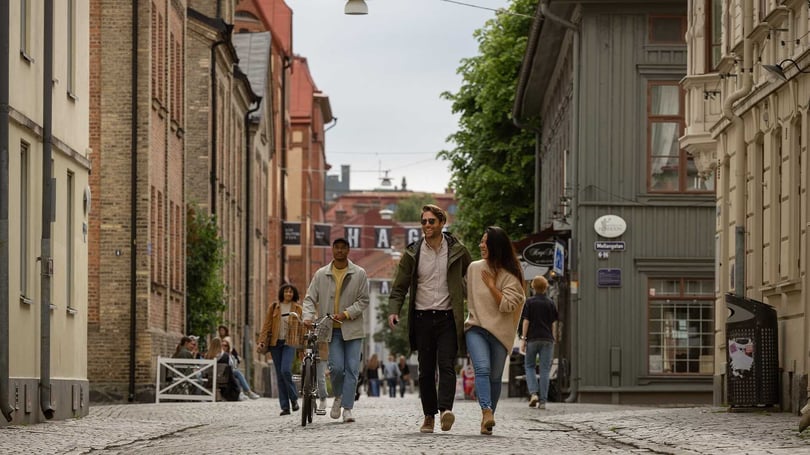 Två personer promenerar tillsammans med en cyklist på en kullerstensgata i Göteborg