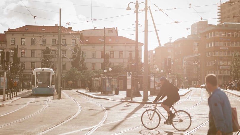 Spårvagn vid en solbelyst stadsgata med cyklist och fotgängare