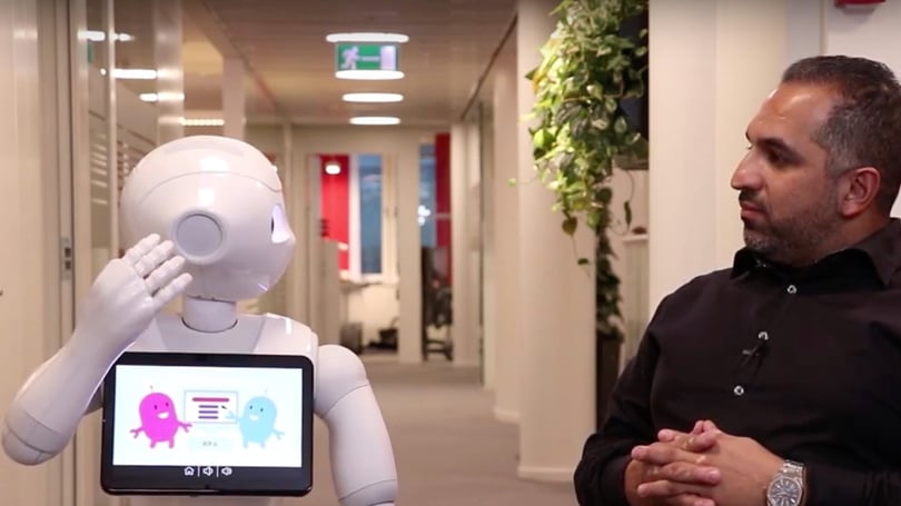 Person in black shirt sitting next to a humanoid robot in a hallway
