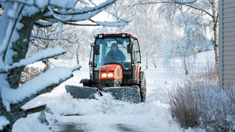 Orange traktor med plog som röjer snö på en väg i vinterlandskap