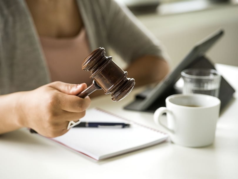 Person som håller i en domarklubba vid ett bord med laptop, anteckningsblock och kaffekopp