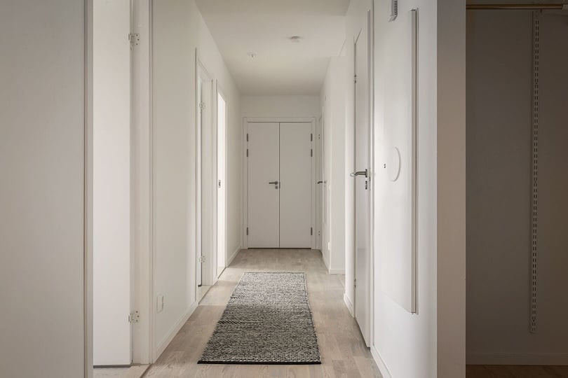 Inflyttningsklar lägenhet med ljus hall, vita väggar och en lång matta på golvet