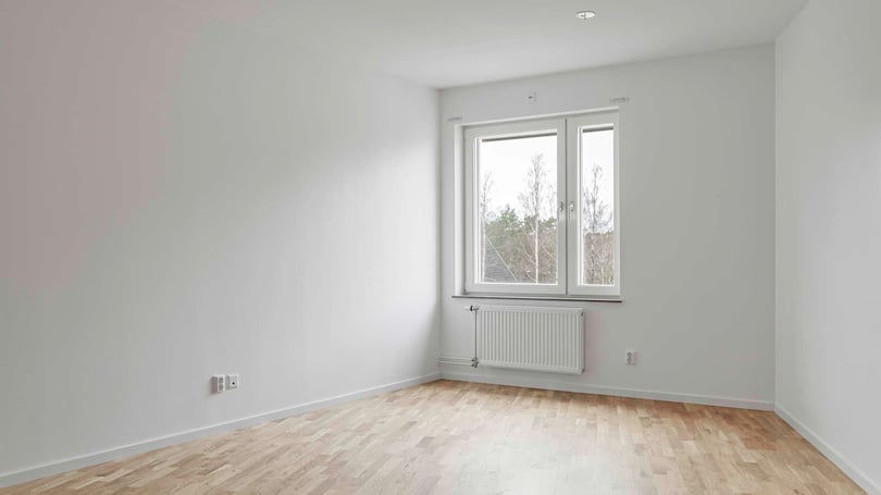 Inflyttningsklart rum med trägolv, vita väggar och fönster med utsikt mot träd