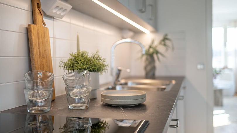 Modernt kök med bänkskiva, diskho, träskärbräda, två glas och en liten växt