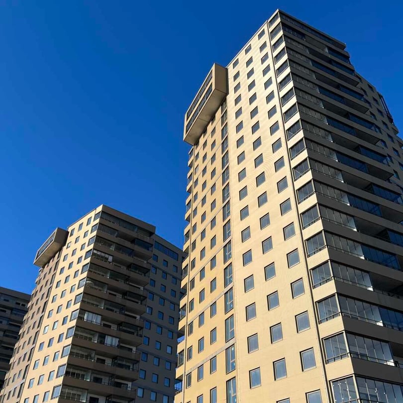 Flerbostadshus med ljus fasad och mörka balkongpartier mot blå himmel