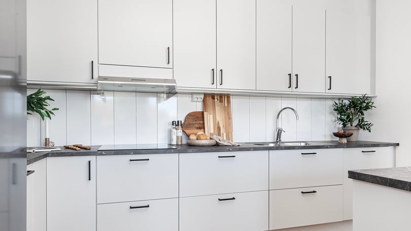 Lägenhet med modernt vitt kök, svarta detaljer och stilren arbetsbänk