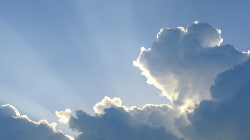 Ljuset bryter igenom stora vita moln mot en blå himmel