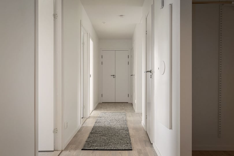 Inflyttningsklar lägenhet med ljus hall, vita väggar och en lång matta på golvet