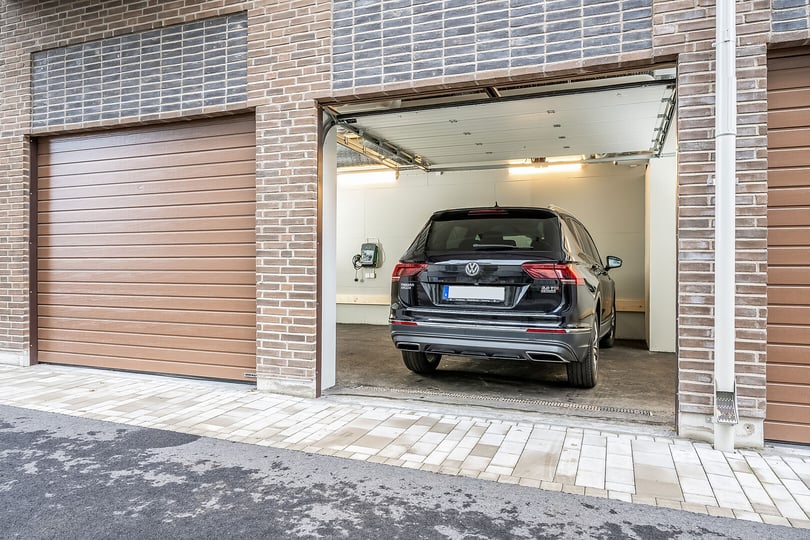 Bil parkerad i en öppen garageport med tegelväggar och omliggande garageportar