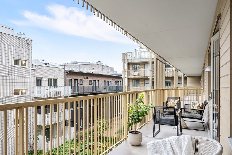 Balkong med utemöbler och en grön växt, omgiven av moderna byggnader under en klar himmel