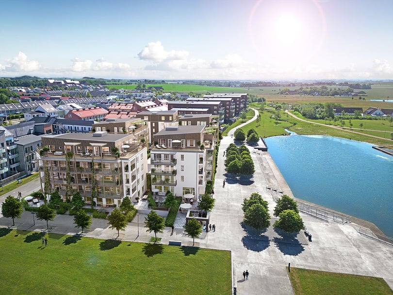 Flygfoto över moderna bostadshus vid vatten med grönområden och gångvägar
