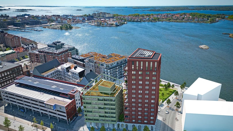 Flygbild över en stad vid vattnet med flera byggnader, inklusive ett höghus, parkeringshus och mindre bostadshus