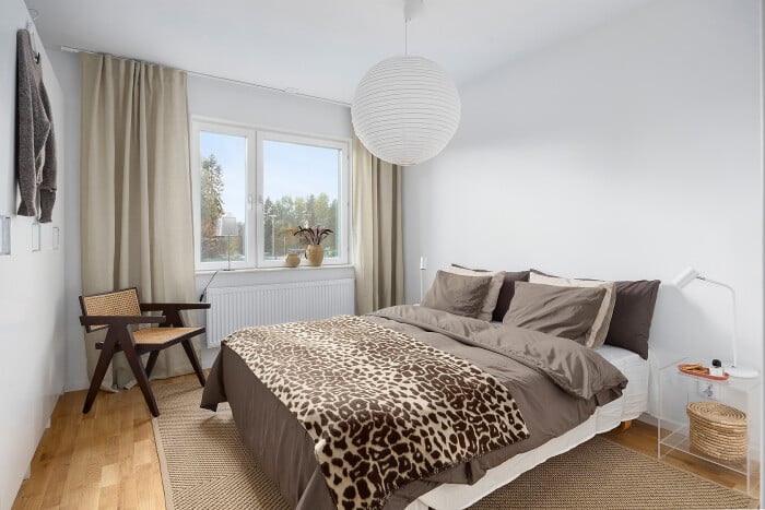 Sovrum med vit vägg, stora fönster, brun sängklädsel med leopardmönster och en rund lampa i taket
