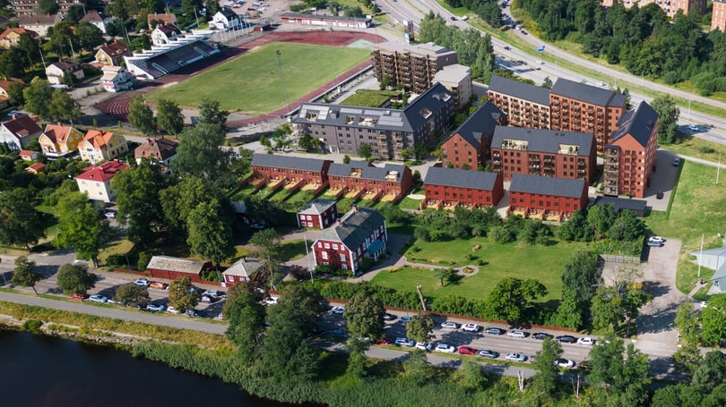 Flygbild över bostadsområde med flerfamiljshus, grönområden och idrottsplats nära vattnet