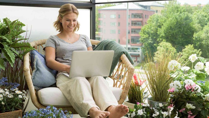 Ung kvinna med laptop på balkong