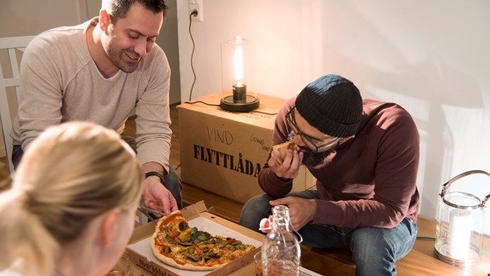 Tre personer äter pizza på en flyttlåda