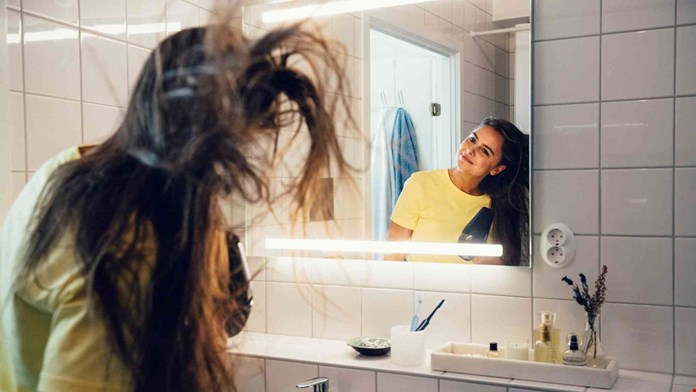 Ung kvinna blåser håret i badrummet