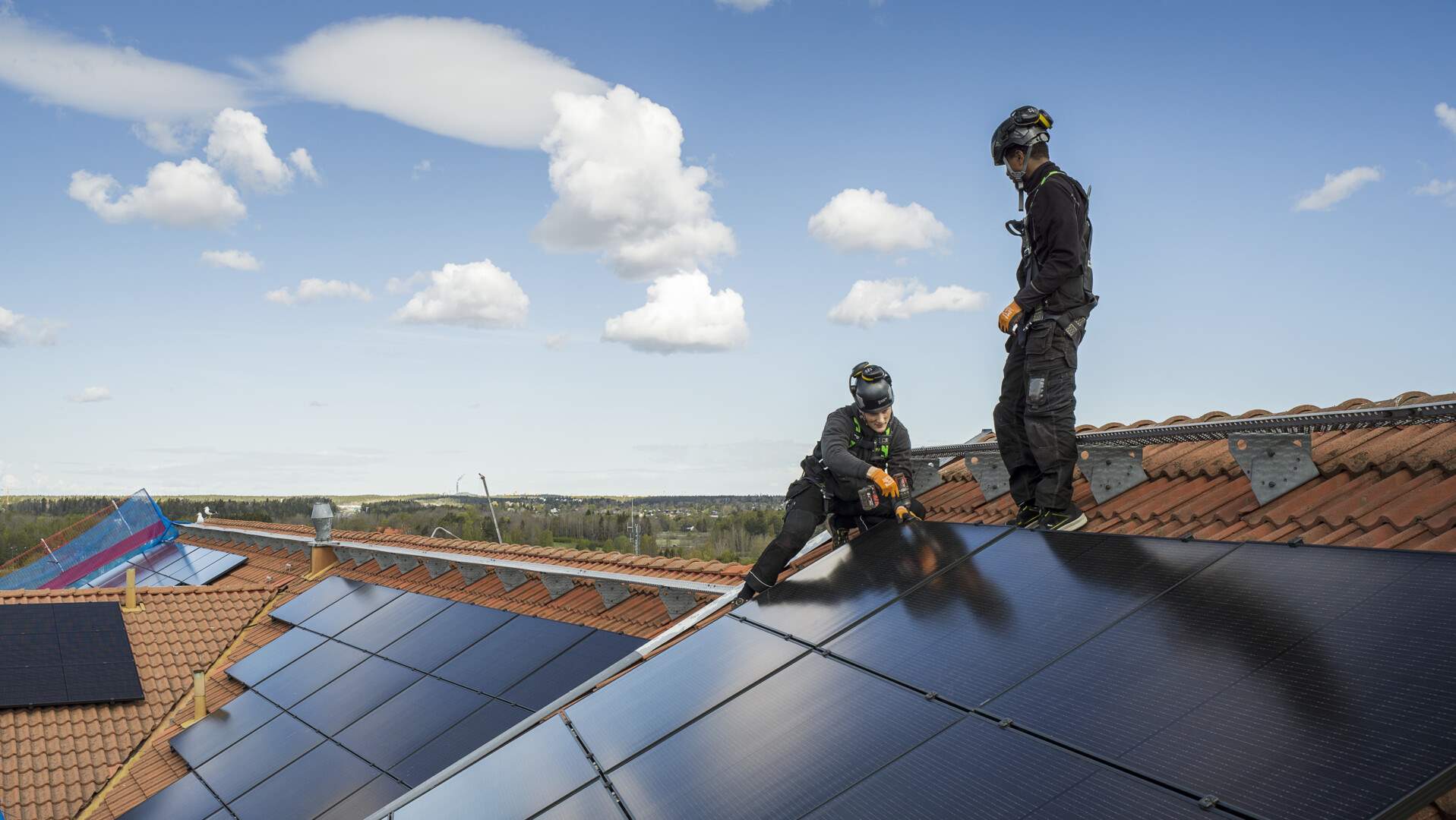 Två medarbetare monterar solceller uppe på takås